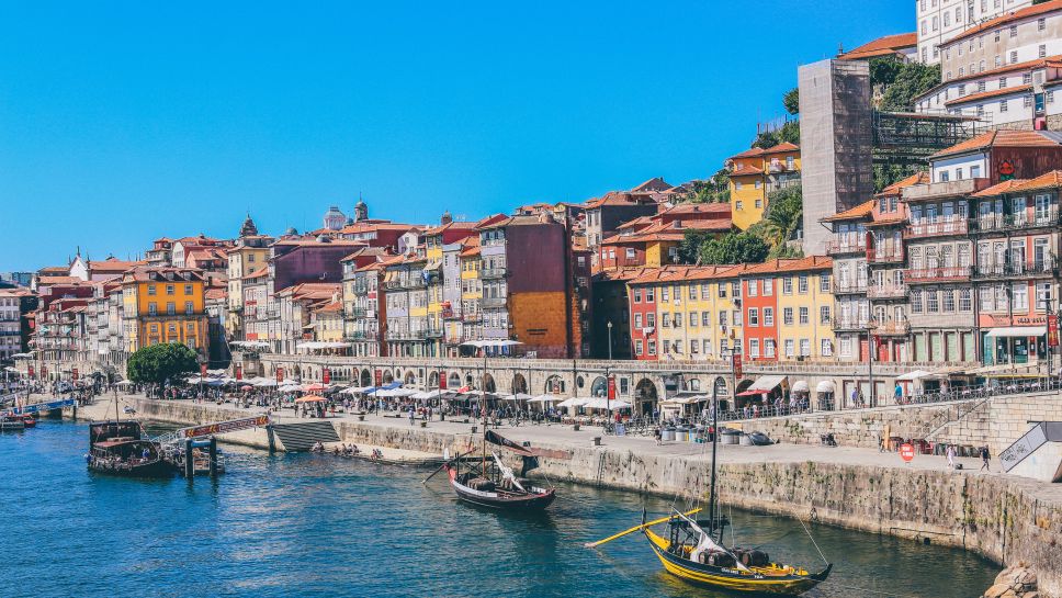 Die belebte Promenade in Porto mit Booten und vielen bunten Häusern.